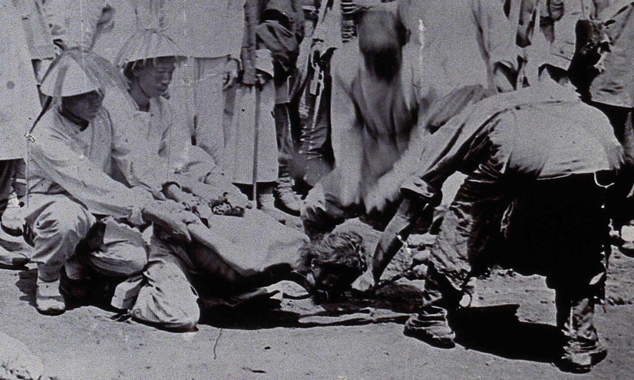 Sword_in_motion_detail,_Man_being_beheaded_in_China,_while_the_body_of_a_man_already_executed_lays_in_the_street_with_three_westerners_in_the_crowd_(cropped).jpg (약혐) 사우디의 망나니가 부족한 이유